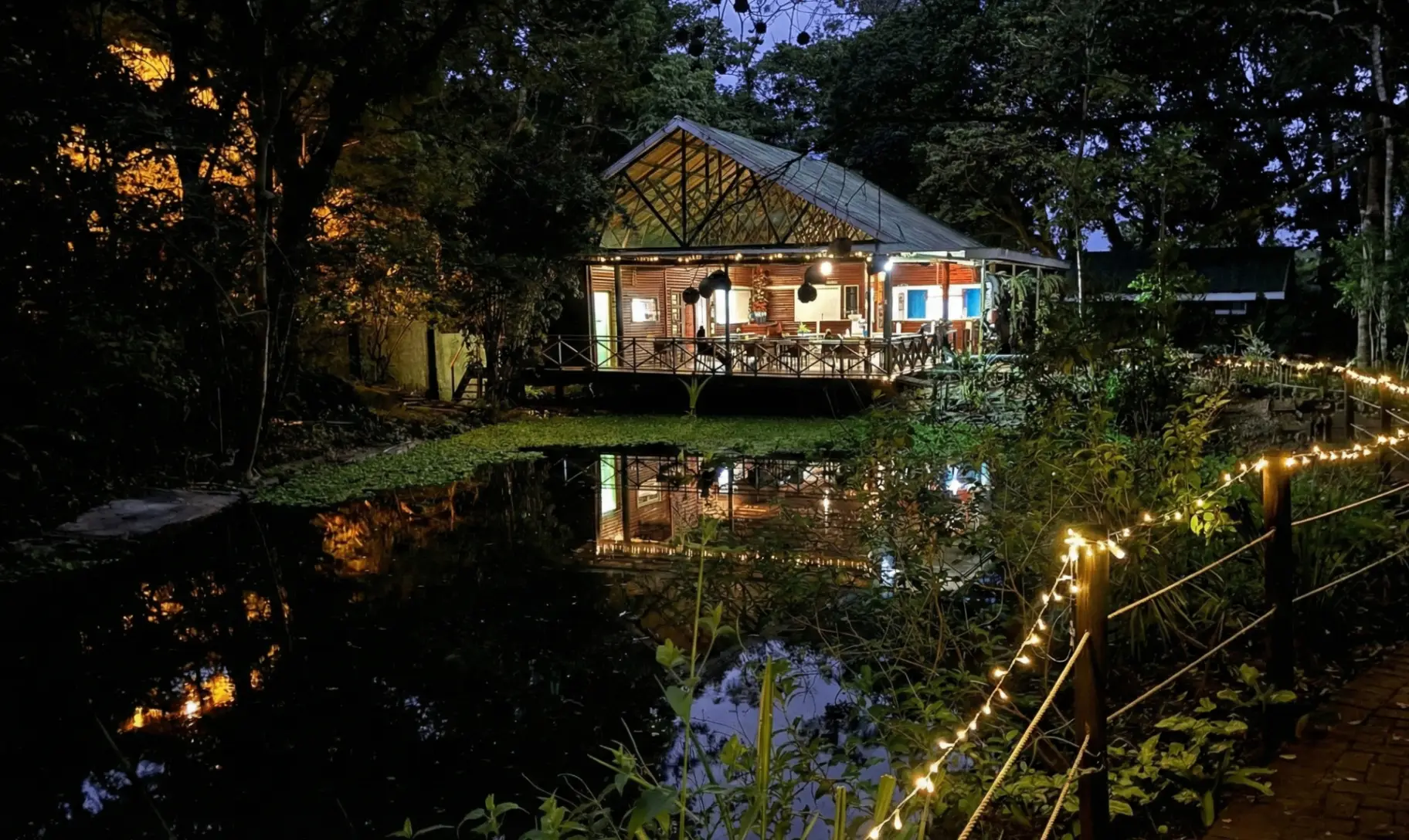 Prana & Bean Café at dusk, its lantern-lit deck reflected in the pond at Marina Beach
